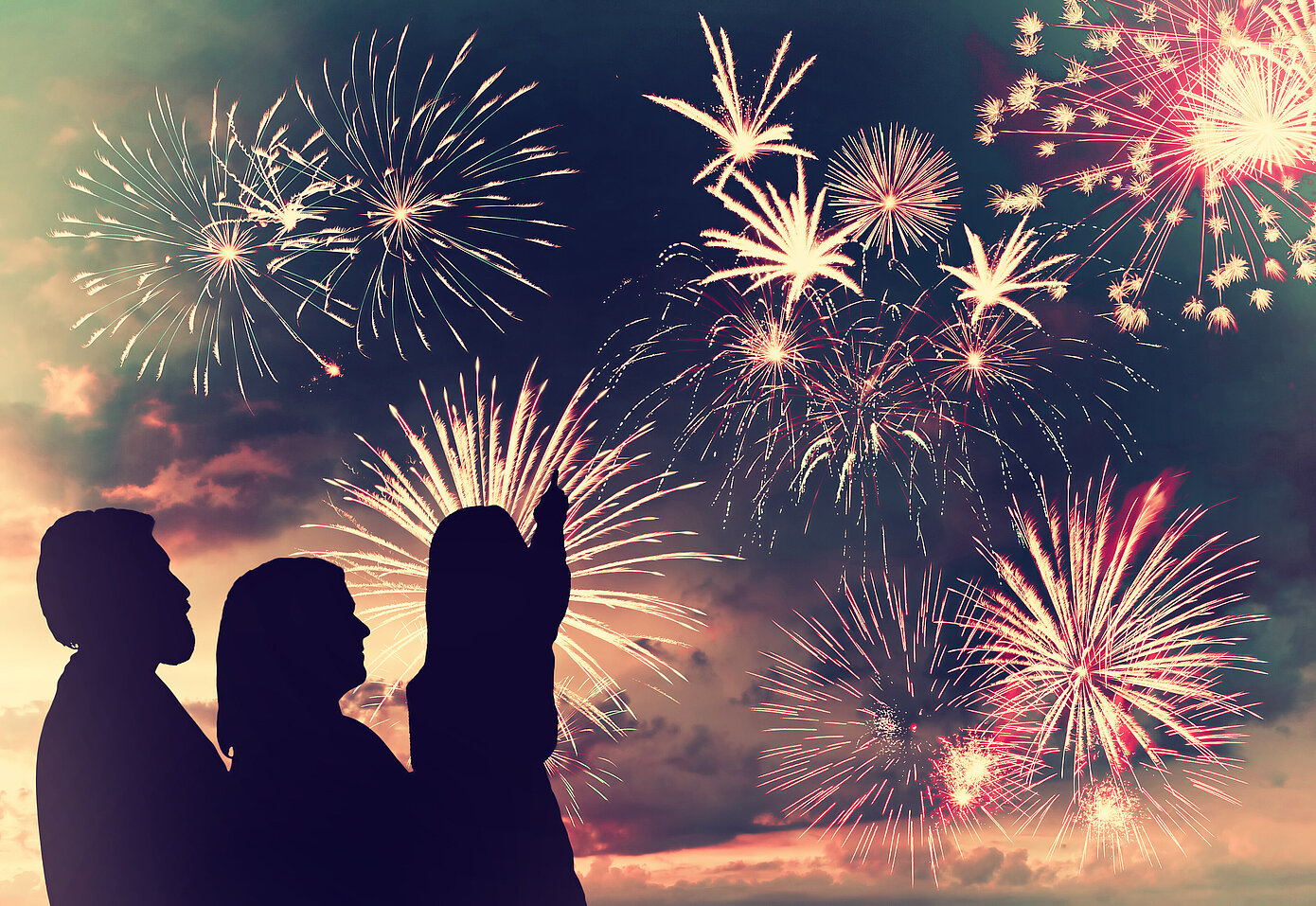 Drei Personen als Silhoutte vor Feuerwerk